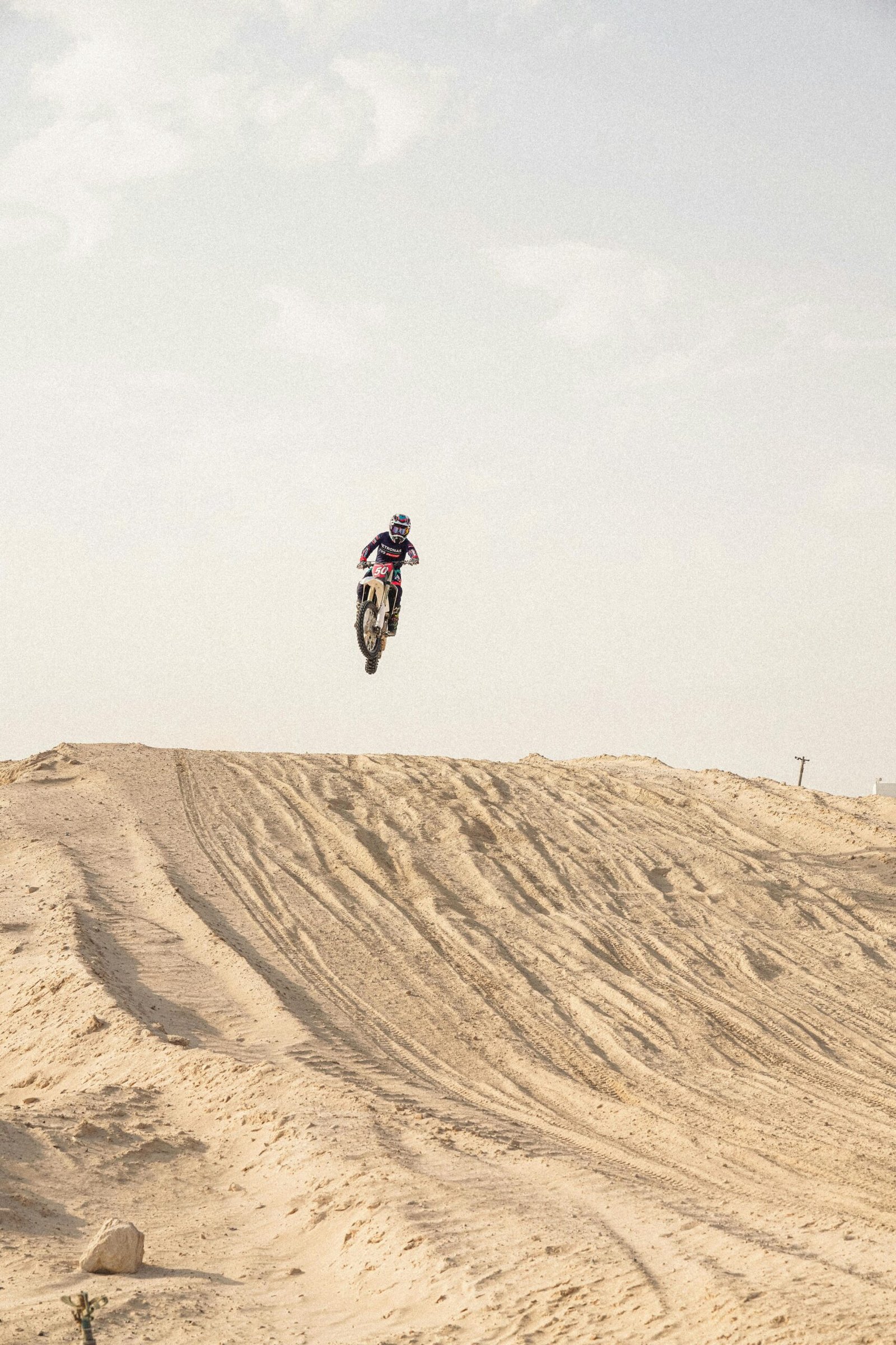 A motocross rider flies over a desert hill, showcasing thrilling riding skills.